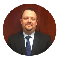 Headshot of Kentucky Farmers Bank SVP/ Chief Operating Officer. He is smirking and wearing a suit and tie against a wooden background